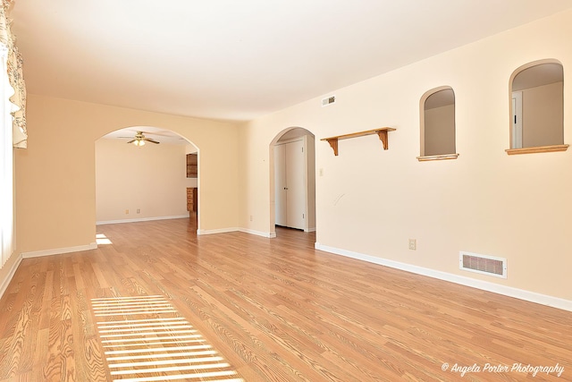 unfurnished room featuring light wood-style floors, visible vents, arched walkways, and baseboards