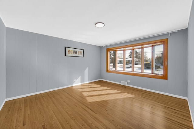 empty room featuring wood finished floors, visible vents, and baseboards