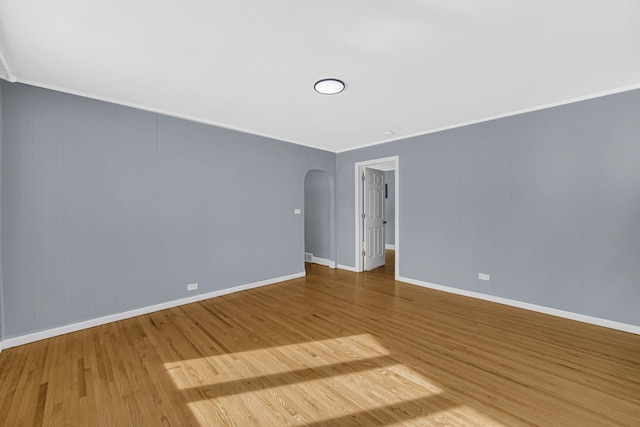 empty room with baseboards, crown molding, arched walkways, and wood finished floors