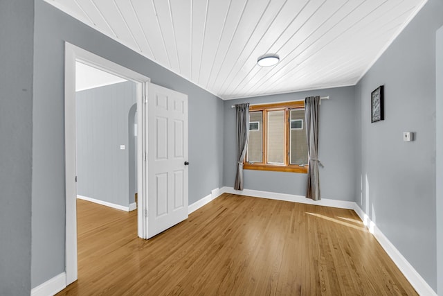 spare room featuring arched walkways, wooden ceiling, baseboards, and wood finished floors