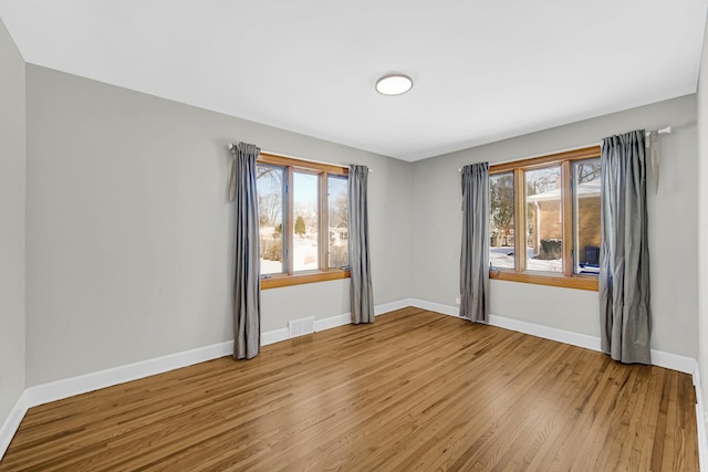 empty room with visible vents, plenty of natural light, baseboards, and wood finished floors