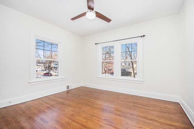 spare room featuring wood finished floors, a ceiling fan, visible vents, baseboards, and ornamental molding