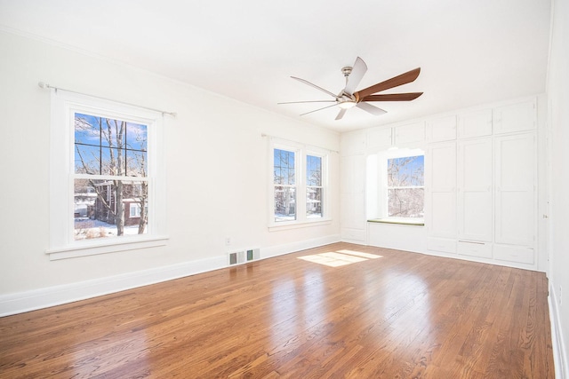 empty room with ceiling fan, wood finished floors, visible vents, and baseboards