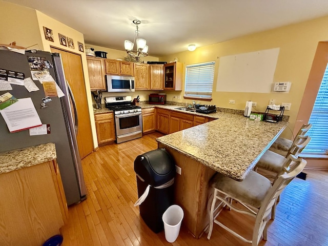 kitchen with stainless steel appliances, brown cabinetry, light wood-type flooring, a peninsula, and a kitchen bar