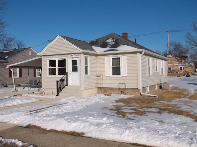 bungalow-style home with entry steps, central air condition unit, a chimney, and roof with shingles