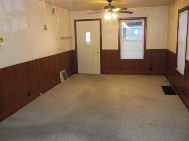 interior space with wainscoting, wood walls, visible vents, and ceiling fan