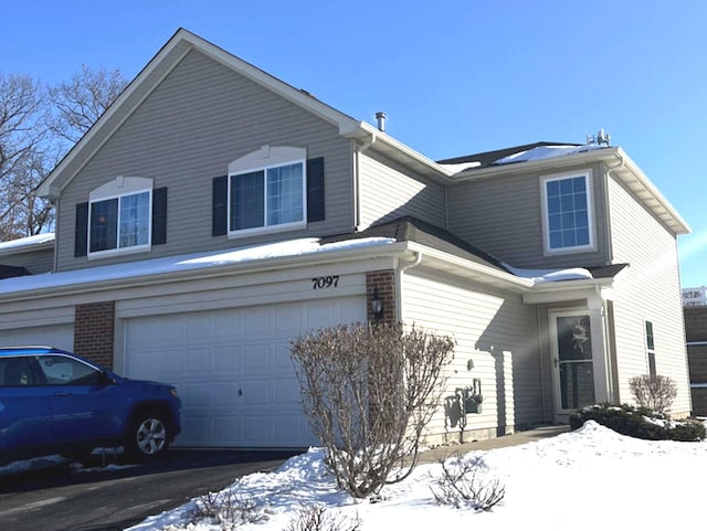 view of snowy exterior featuring brick siding, driveway, and an attached garage