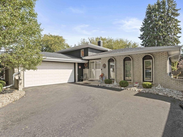 view of front of property featuring an attached garage, a chimney, aphalt driveway, and brick siding