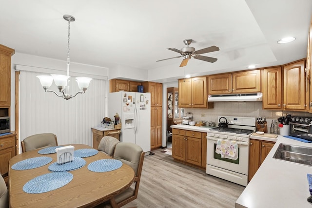 kitchen with pendant lighting, brown cabinets, light countertops, white appliances, and under cabinet range hood