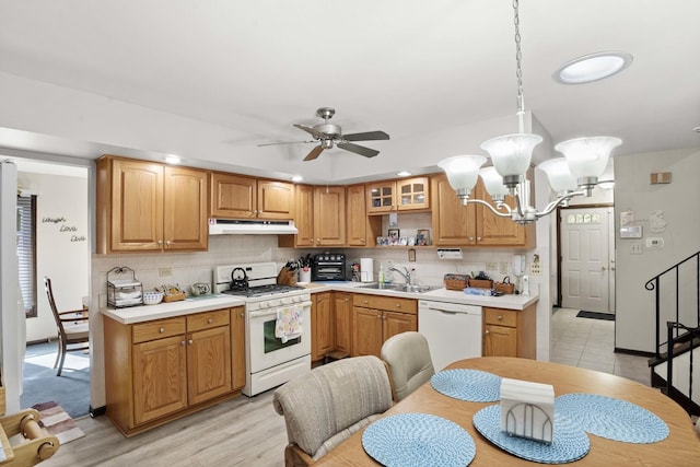 kitchen with white appliances, glass insert cabinets, decorative light fixtures, light countertops, and under cabinet range hood