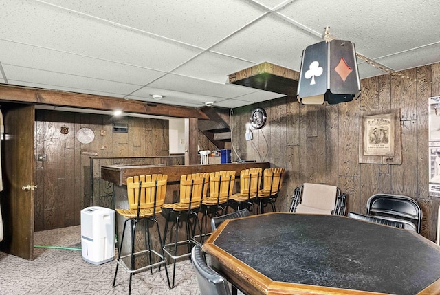 game room featuring a bar, carpet, wooden walls, and a drop ceiling