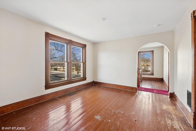 unfurnished room with arched walkways, visible vents, baseboards, and wood finished floors