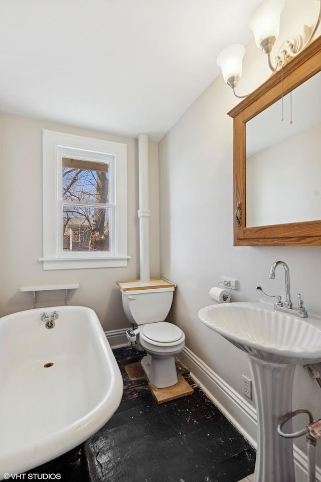 full bath with toilet, a freestanding bath, and baseboards