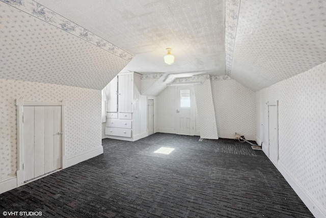 additional living space featuring lofted ceiling, wallpapered walls, baseboards, and dark carpet