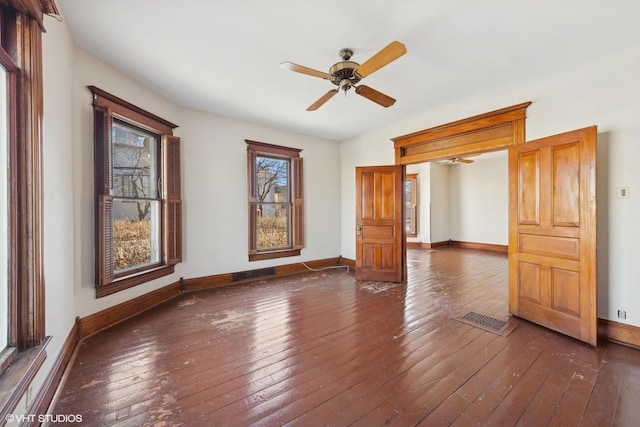 spare room with dark wood-type flooring, visible vents, ceiling fan, and baseboards