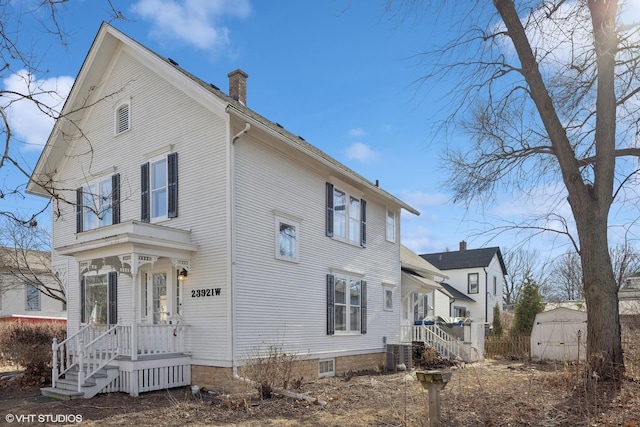 view of side of property featuring central AC, a chimney, and a storage unit