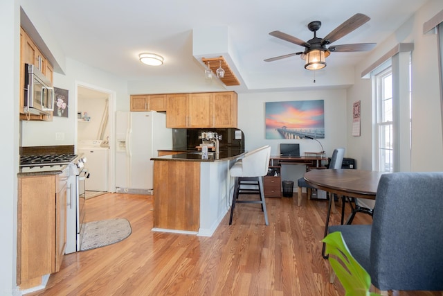 kitchen featuring dark countertops, light wood-style flooring, a peninsula, stainless steel appliances, and a kitchen bar