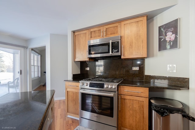 kitchen with tasteful backsplash, baseboards, appliances with stainless steel finishes, dark stone countertops, and light wood-type flooring