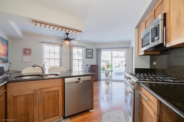 kitchen featuring stainless steel appliances, dark countertops, a sink, and brown cabinets