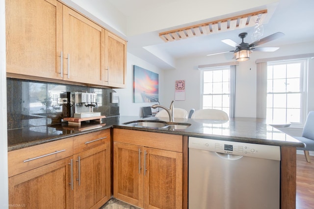 kitchen with a peninsula, a sink, dishwasher, tasteful backsplash, and dark countertops