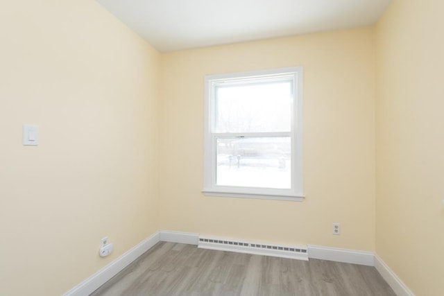 empty room with a baseboard heating unit, light wood finished floors, and baseboards