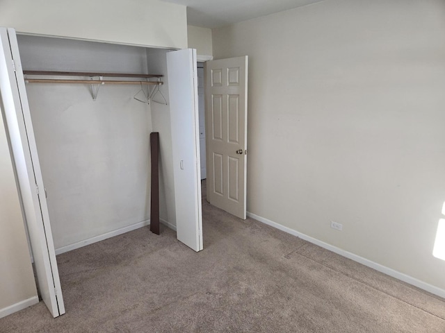 unfurnished bedroom with a closet, light carpet, and baseboards