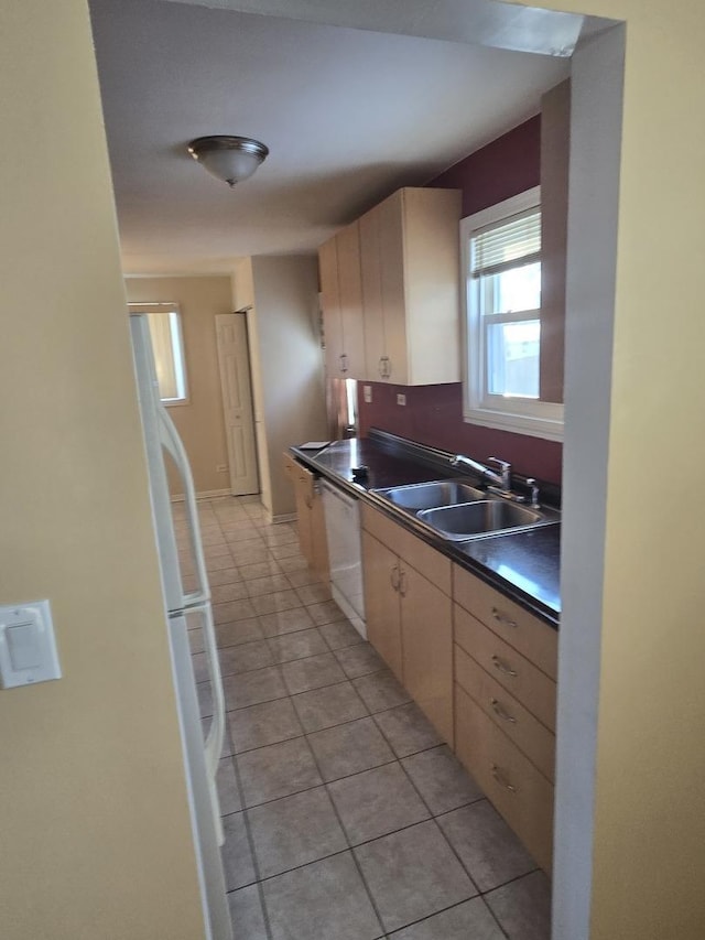 kitchen with dark countertops, dishwasher, a sink, and light tile patterned floors