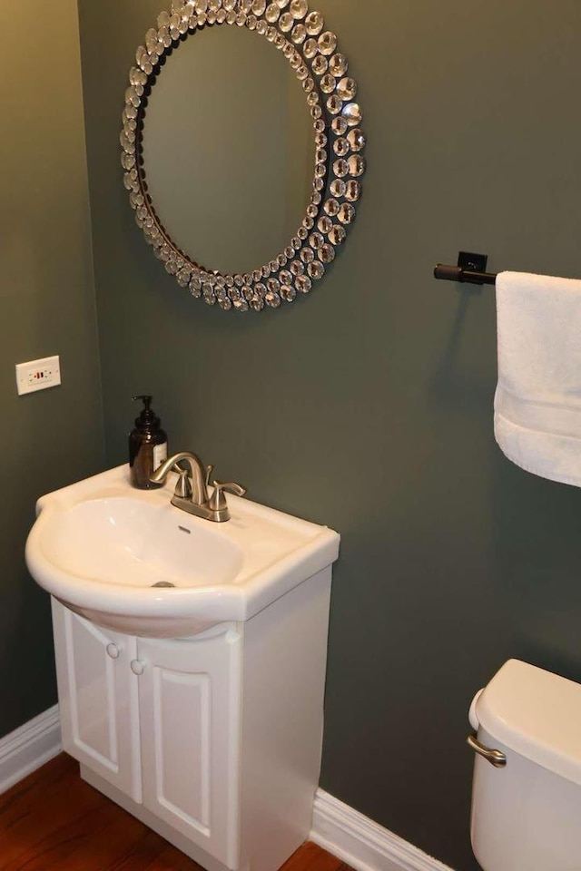 bathroom with toilet, vanity, baseboards, and wood finished floors