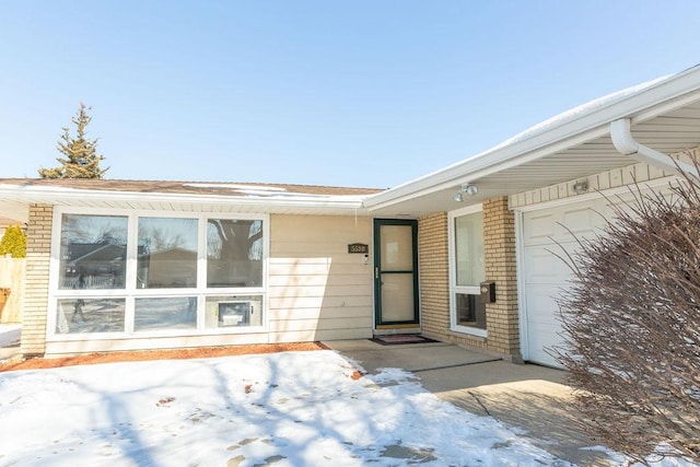 snow covered property entrance featuring a garage and brick siding