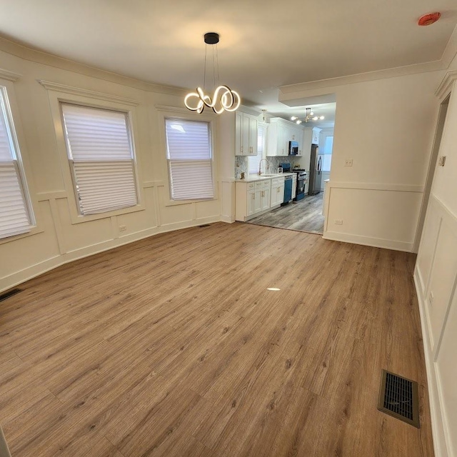 unfurnished dining area featuring light wood finished floors, visible vents, a decorative wall, and a notable chandelier