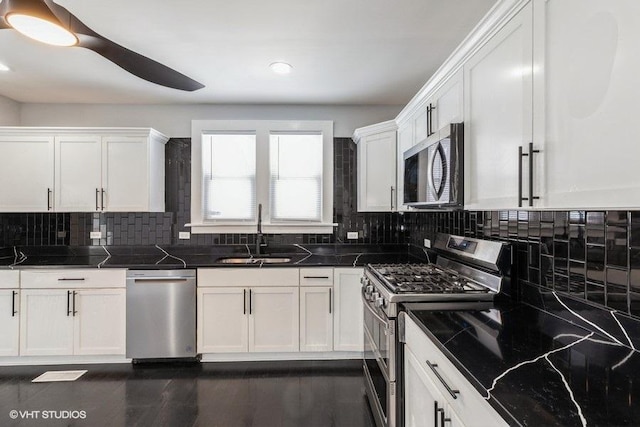 kitchen featuring white cabinets, dark stone countertops, stainless steel appliances, and a sink