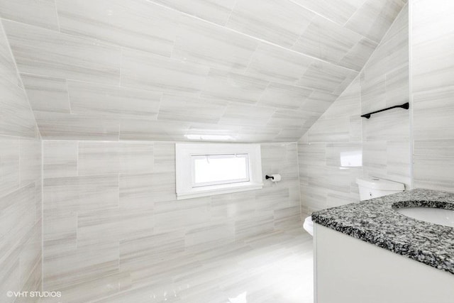 bathroom featuring lofted ceiling, toilet, vanity, and tile walls