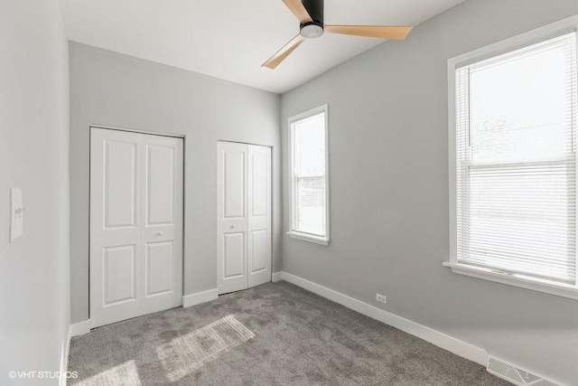 unfurnished bedroom featuring two closets, light colored carpet, visible vents, ceiling fan, and baseboards