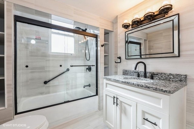 bathroom with toilet, bath / shower combo with glass door, vanity, and tile walls