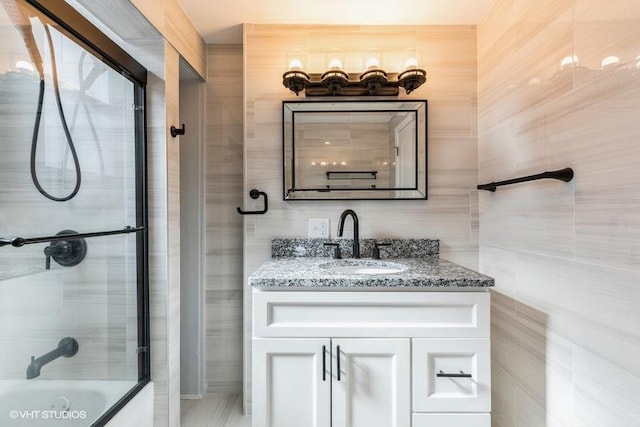 bathroom with combined bath / shower with glass door, vanity, and tile walls