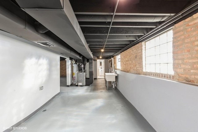 basement with brick wall, a sink, visible vents, water heater, and heating unit