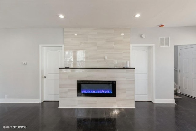 unfurnished living room with baseboards, visible vents, dark wood-type flooring, a fireplace, and recessed lighting