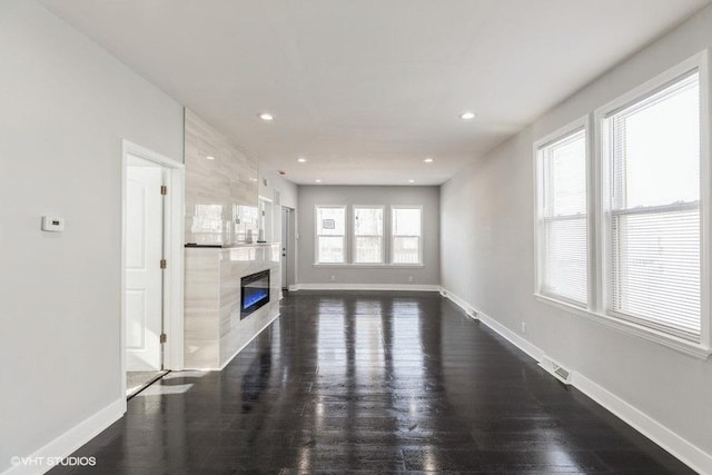 unfurnished living room with dark wood-style flooring, recessed lighting, visible vents, a premium fireplace, and baseboards