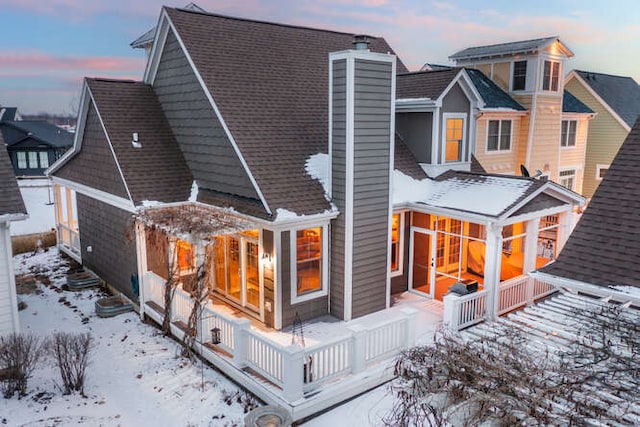 snow covered rear of property with a shingled roof, a sunroom, and a chimney