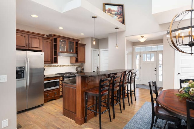 kitchen featuring pendant lighting, dark countertops, appliances with stainless steel finishes, glass insert cabinets, and light wood-type flooring