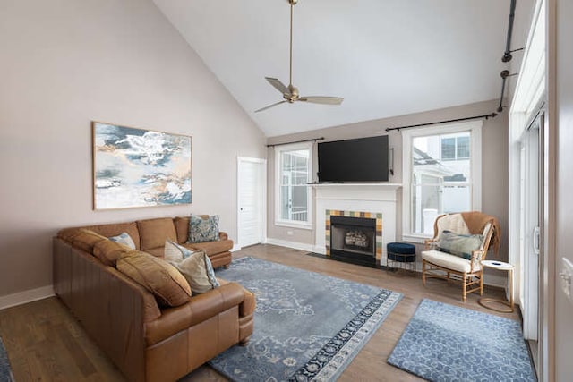 living area featuring baseboards, a tiled fireplace, dark wood-style floors, ceiling fan, and high vaulted ceiling