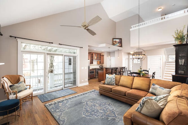 living area with ceiling fan with notable chandelier, high vaulted ceiling, wood finished floors, and baseboards