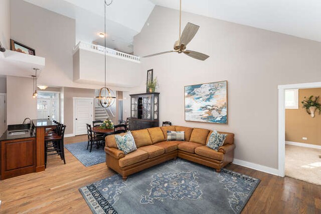 living area with high vaulted ceiling, wood finished floors, ceiling fan, and stairs