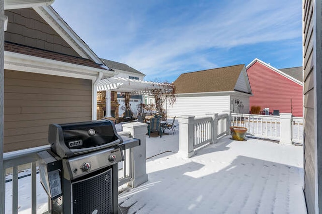 snow covered patio with grilling area, a wooden deck, and a pergola