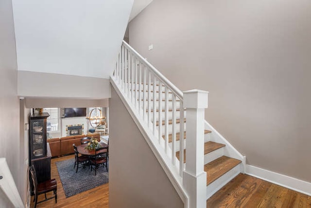 staircase with a fireplace, a towering ceiling, baseboards, and wood finished floors