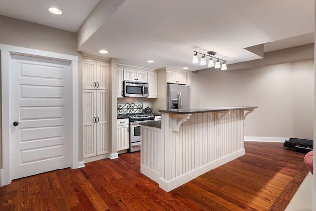 kitchen with dark countertops, a breakfast bar, dark wood-style flooring, stainless steel appliances, and white cabinetry