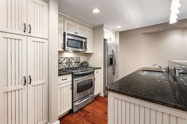 kitchen featuring stainless steel appliances, dark wood-type flooring, a sink, white cabinets, and dark stone countertops