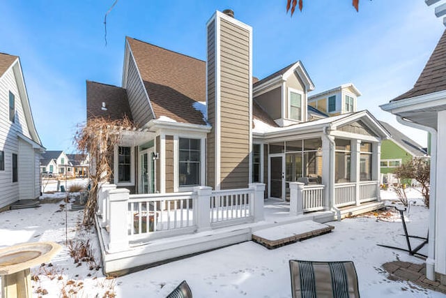 snow covered rear of property featuring a sunroom and a chimney