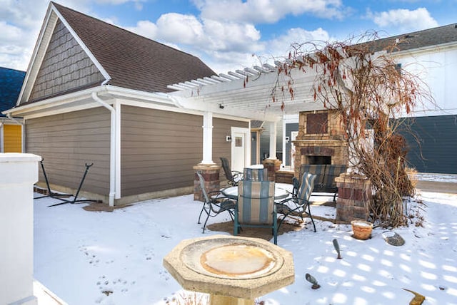 snow covered patio with an outdoor stone fireplace and a pergola