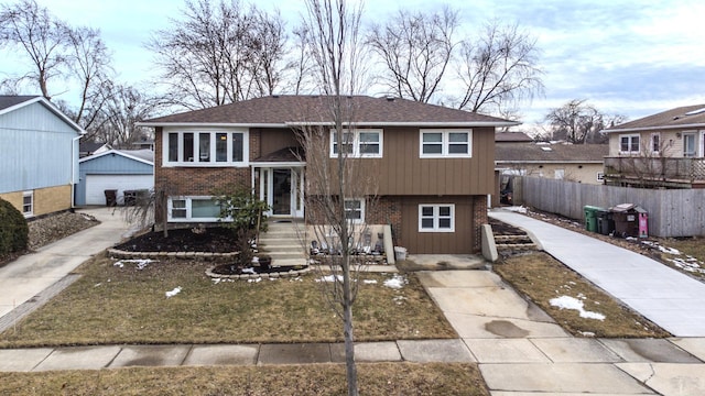 bi-level home with a detached garage, fence, an outdoor structure, and brick siding